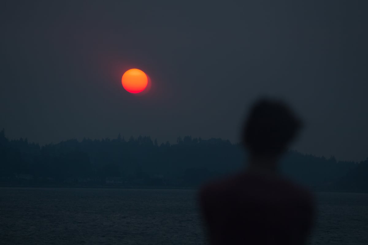 A forest-fire-red sun hangs over the Salish Sea from the BC Ferry between Vancouver and Nanaimo, with a quiet figure watching from shore. print option