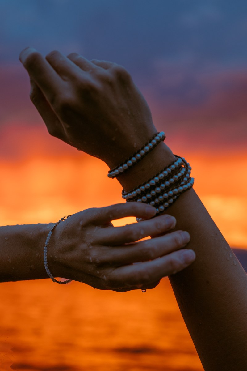 Hands and bracelets catch a stunning orange sunset over Okanagan Lake at Bertram Park in Kelowna. print option
