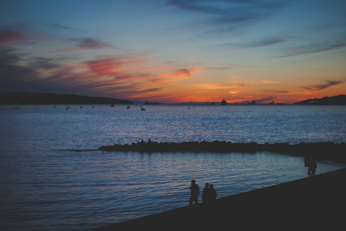 Blue and rose sunset colour over English Bay with tiny figures on the shore. print option