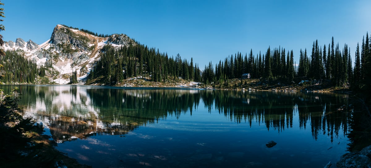 A long alpine lake panorama with dark trees mirrored in still water. print option