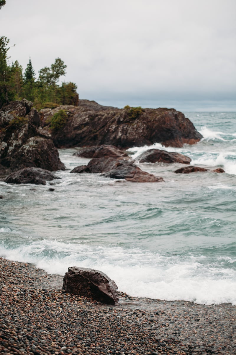 Lake Huron waves break around a dark rock shelf and forested edge. print option