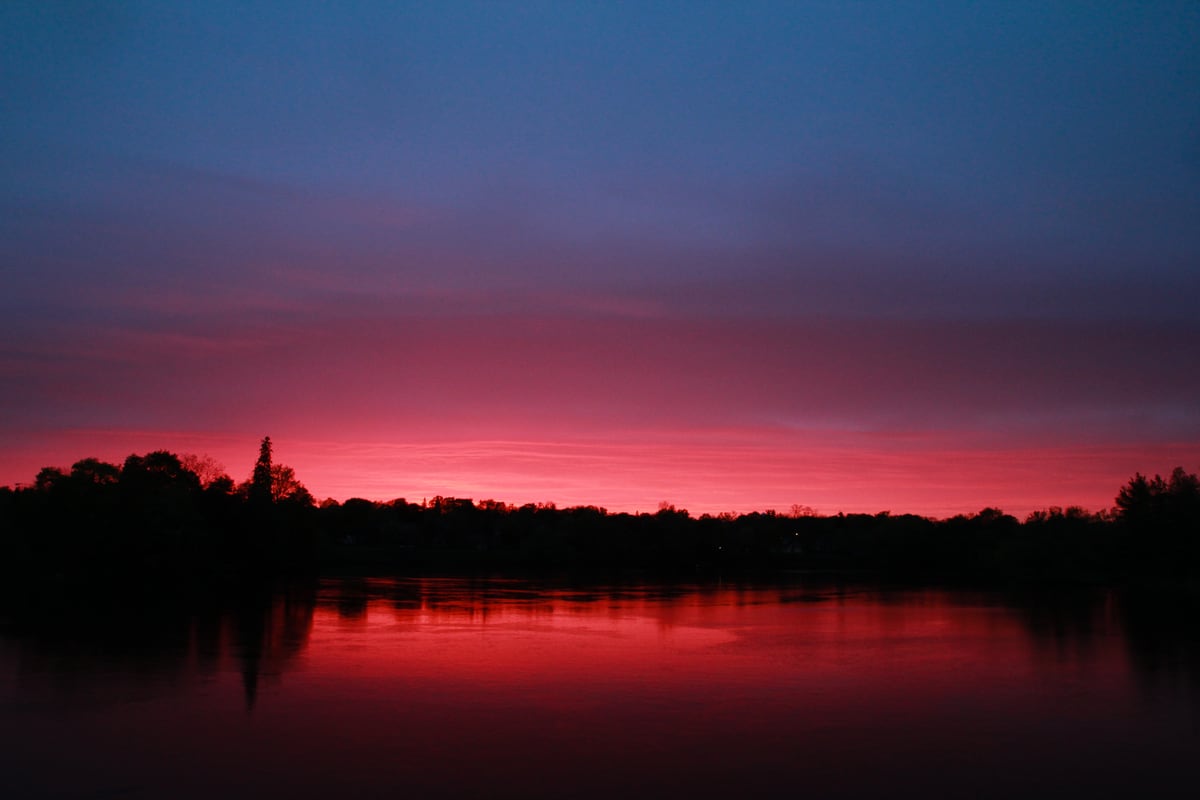 A magenta lake sunset reflects against a dark Peterborough tree line. print option