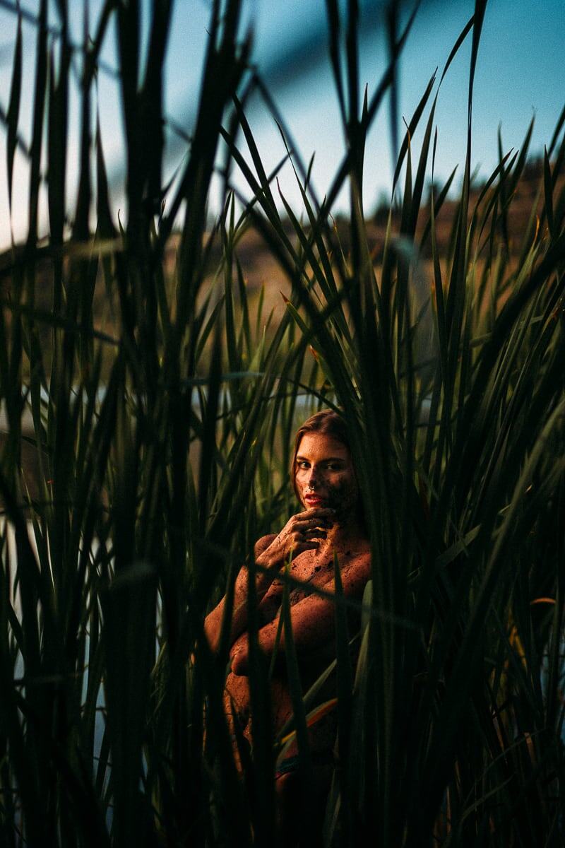 Mo in the Reeds story frame 16: Green shadow, tall grass, body paint and a charged quiet that stays grounded in portrait atmosphere.