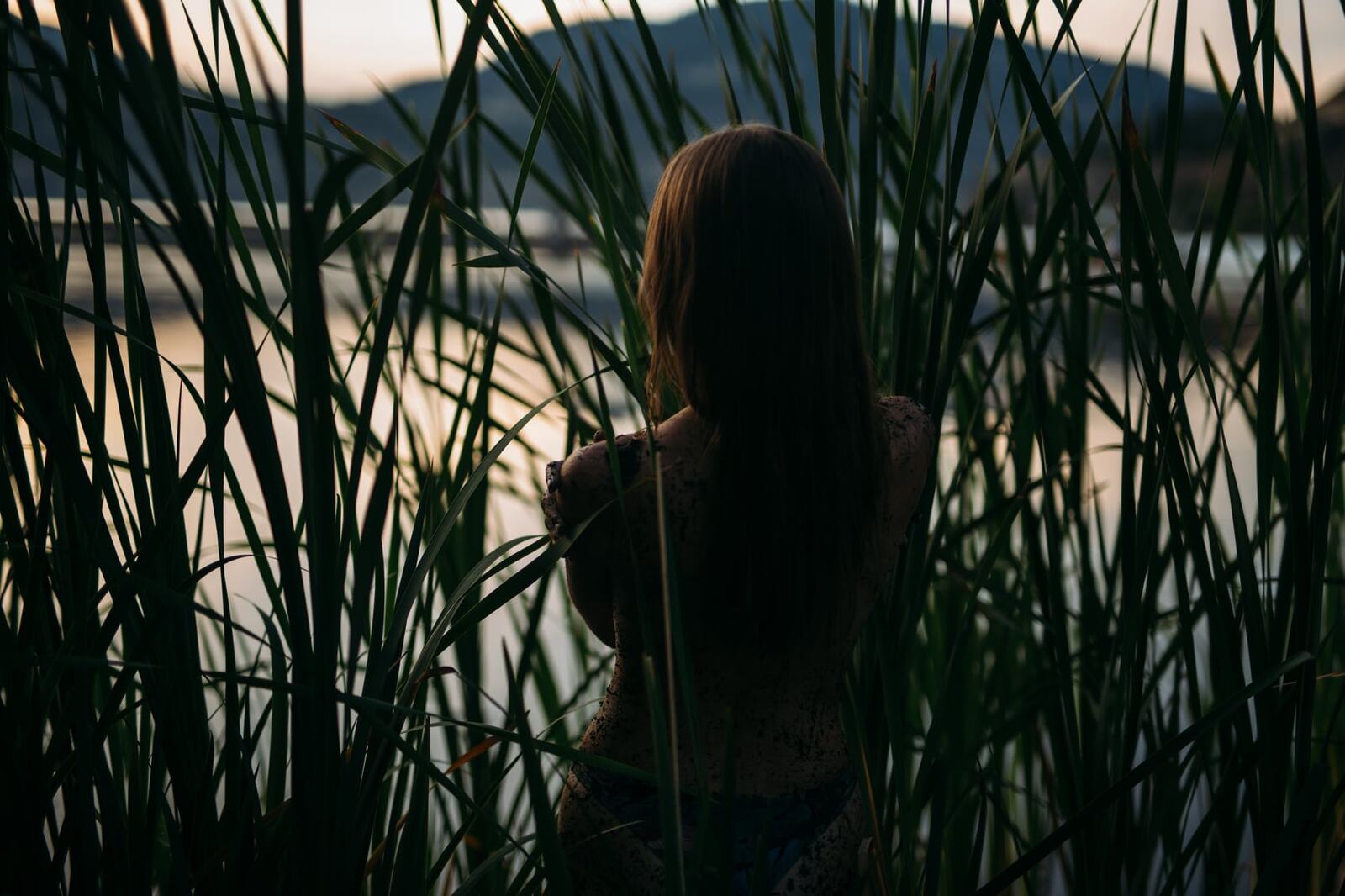 Mo in the Reeds story frame 15: Green shadow, tall grass, body paint and a charged quiet that stays grounded in portrait atmosphere.