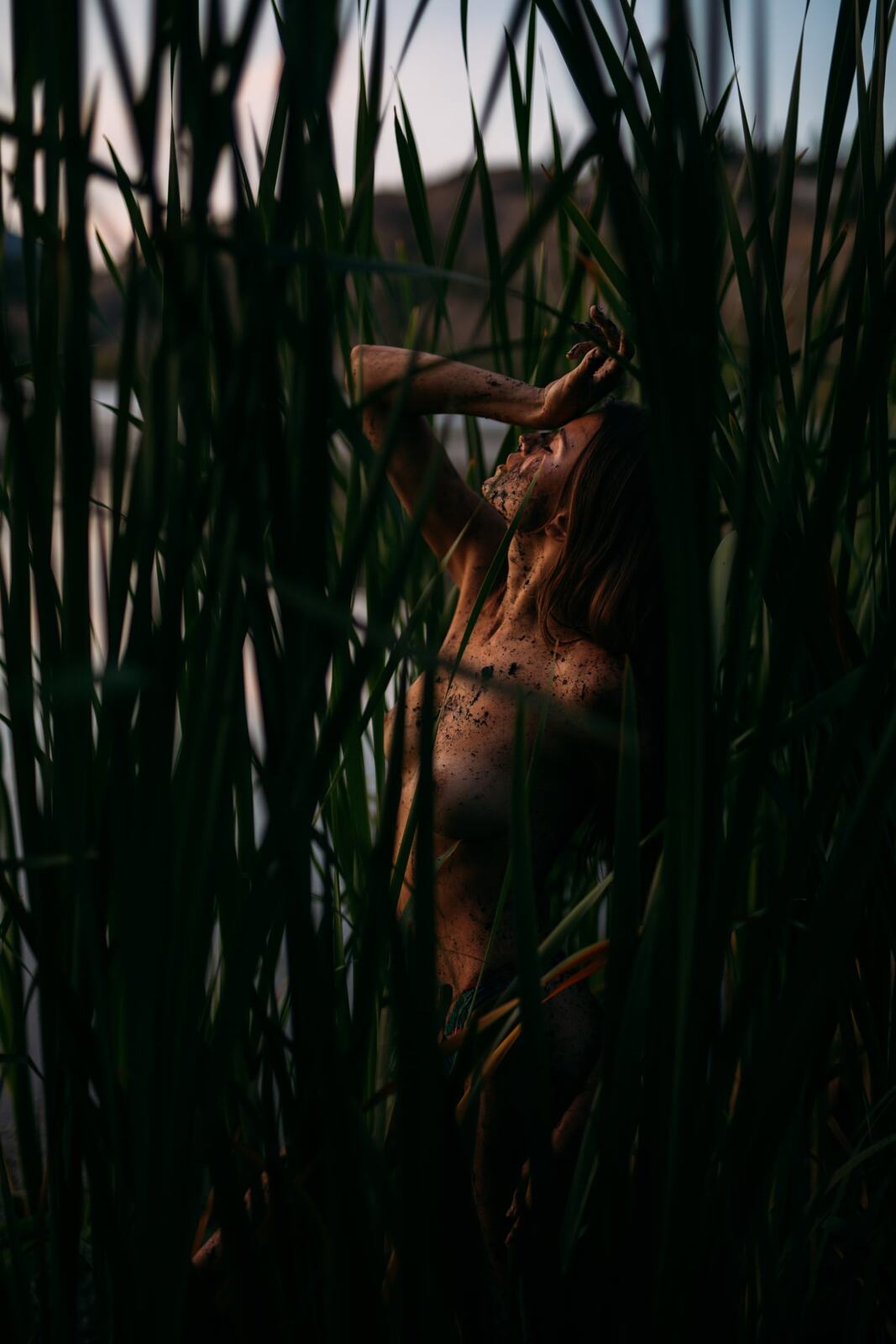 Mo in the Reeds story frame 17: Green shadow, tall grass, body paint and a charged quiet that stays grounded in portrait atmosphere.