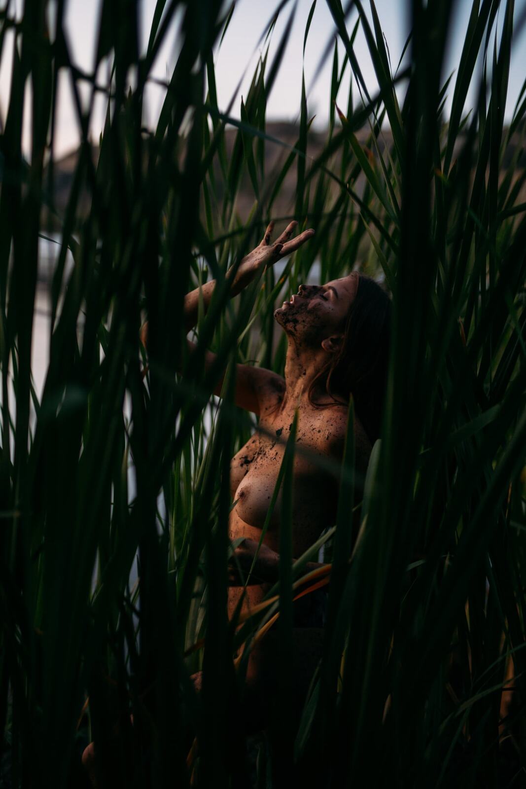 Mo in the Reeds story frame 18: Green shadow, tall grass, body paint and a charged quiet that stays grounded in portrait atmosphere.