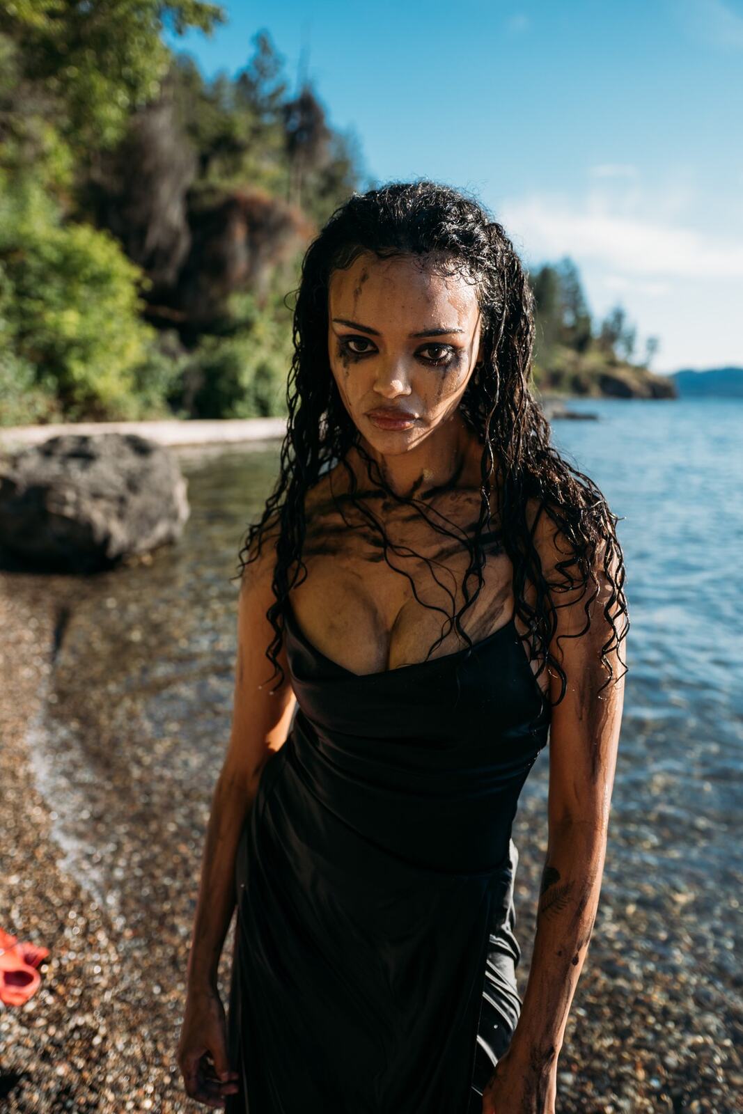 Alex by the Lake portraits story frame 8: Okanagan Lake portraits in Kelowna with black styling, rock, water, wind, direct expression and a cinematic beauty-portrait edge.