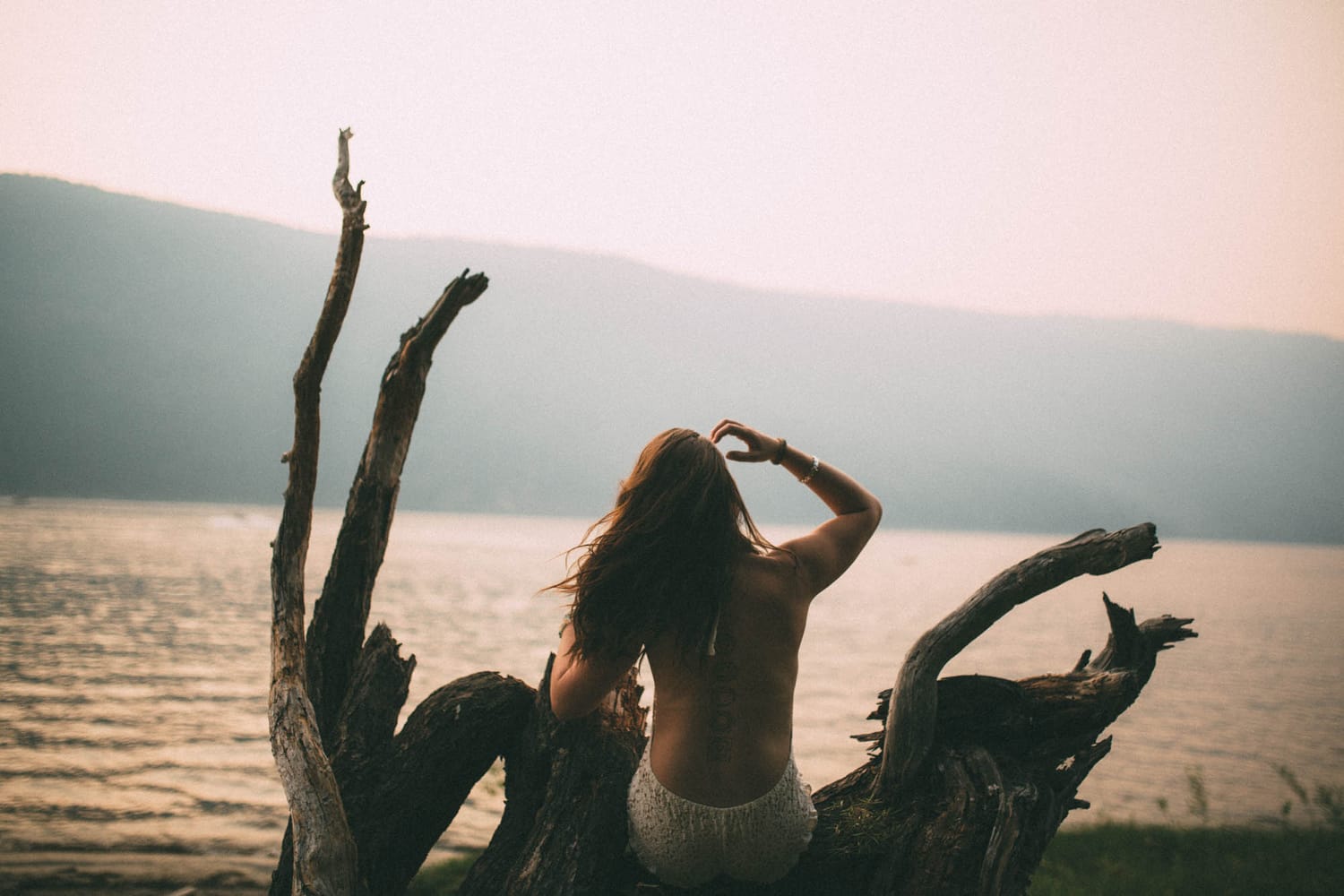 Erin at Mara Lake portraits story frame 3: Mara Lake portraits for Erin with driftwood, warm water, tattoo detail and soft evening light across the Shuswap shoreline.