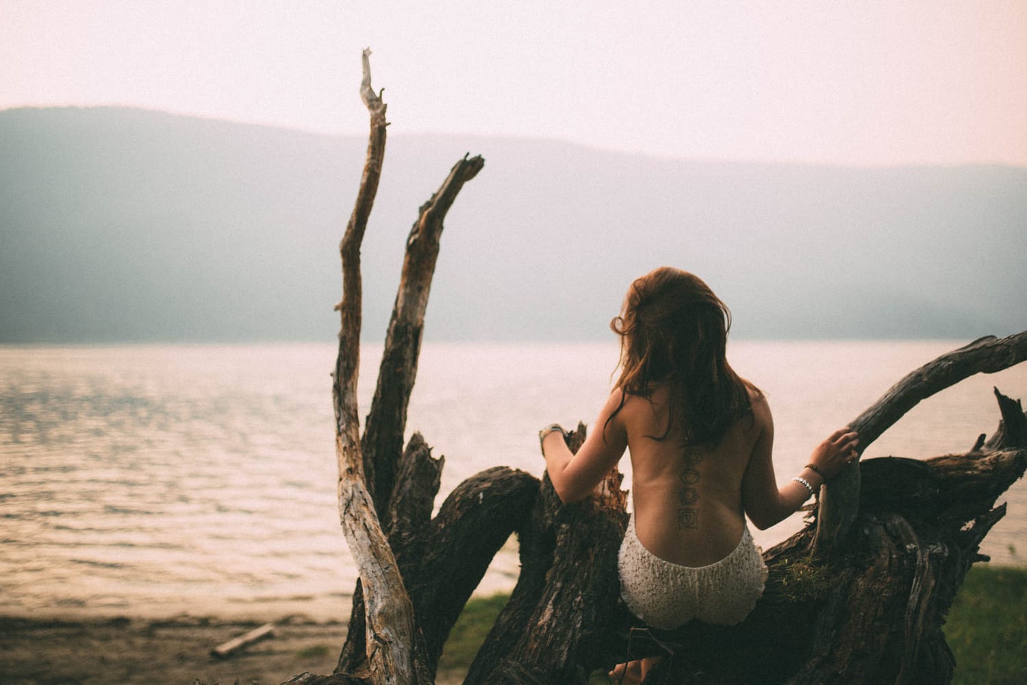 Erin at Mara Lake portraits story frame 5: Mara Lake portraits for Erin with driftwood, warm water, tattoo detail and soft evening light across the Shuswap shoreline.