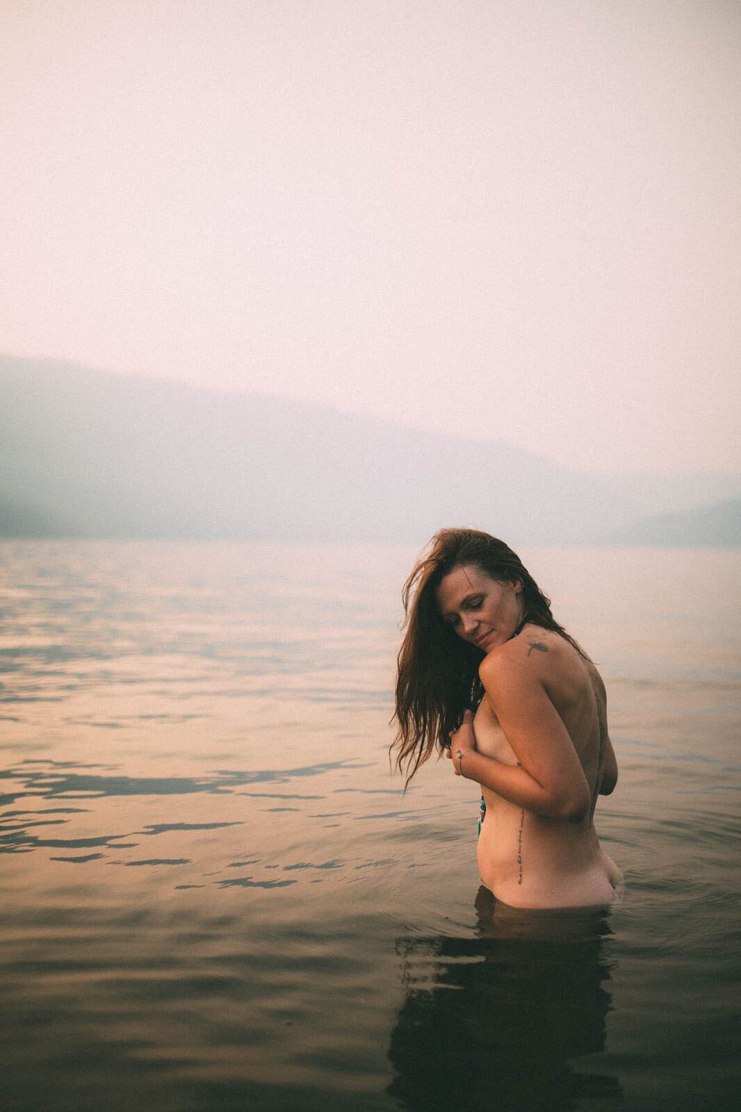 Erin at Mara Lake portraits story frame 9: Mara Lake portraits for Erin with driftwood, warm water, tattoo detail and soft evening light across the Shuswap shoreline.