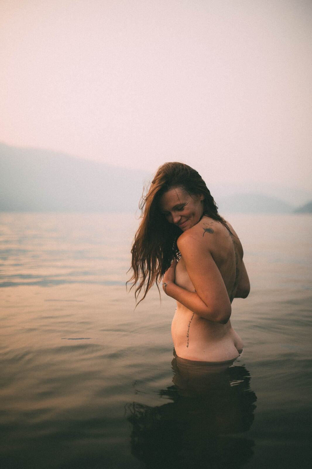 Erin at Mara Lake portraits story frame 10: Mara Lake portraits for Erin with driftwood, warm water, tattoo detail and soft evening light across the Shuswap shoreline.
