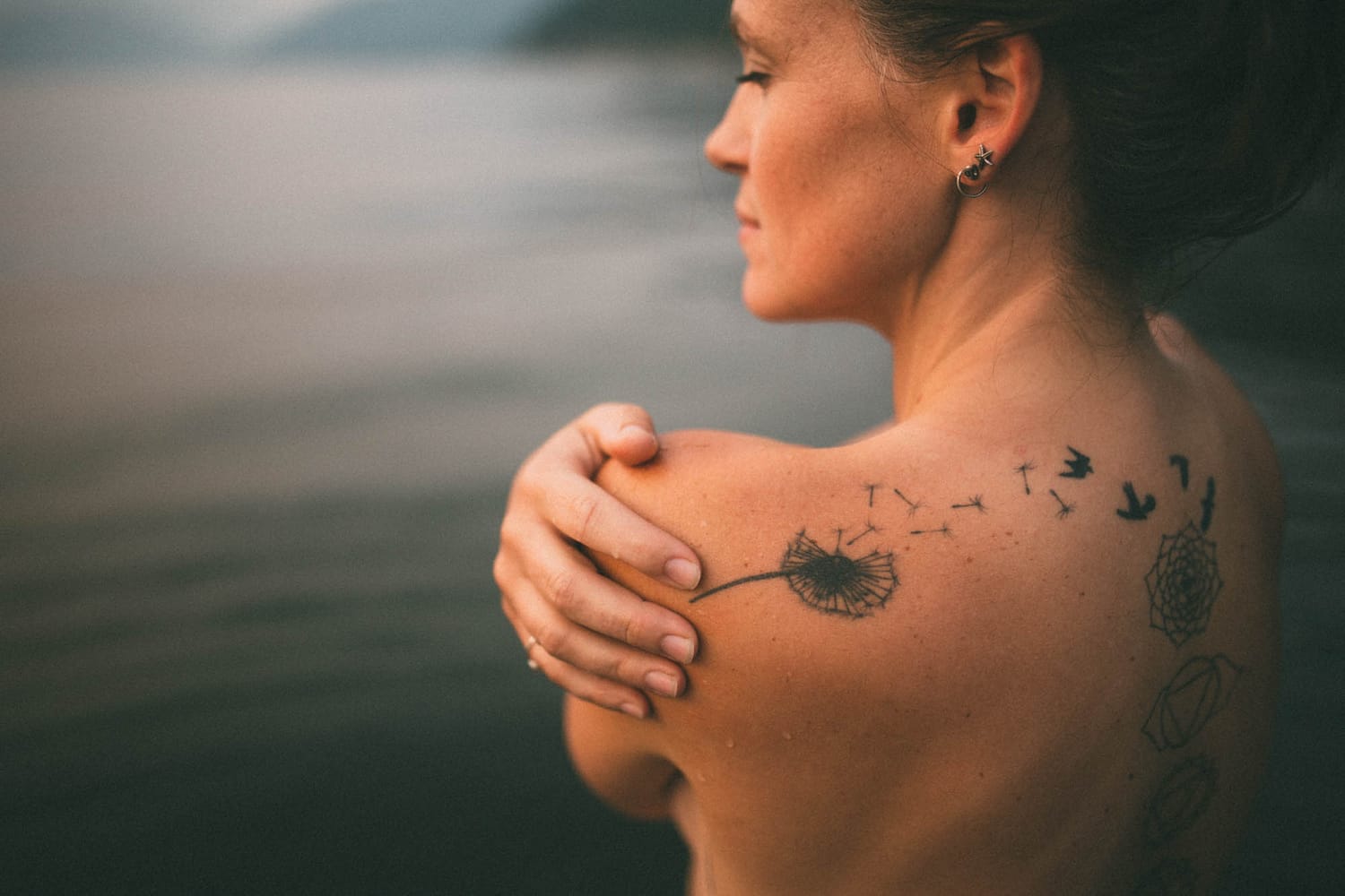 Erin at Mara Lake portraits story frame 11: Mara Lake portraits for Erin with driftwood, warm water, tattoo detail and soft evening light across the Shuswap shoreline.