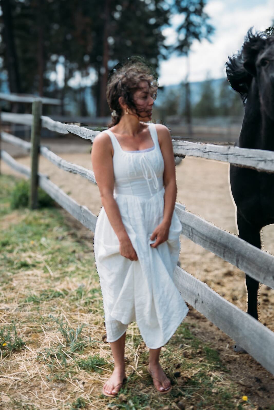 Giuliana at LoveReins portraits story frame 5: Equestrian portrait session at Love Reins Ranch in Lake Country, BC, with Giuliana, horses, white-dress portraits, Western cowgirl styling, ranch fencing, riding frames and warm Okanagan light..