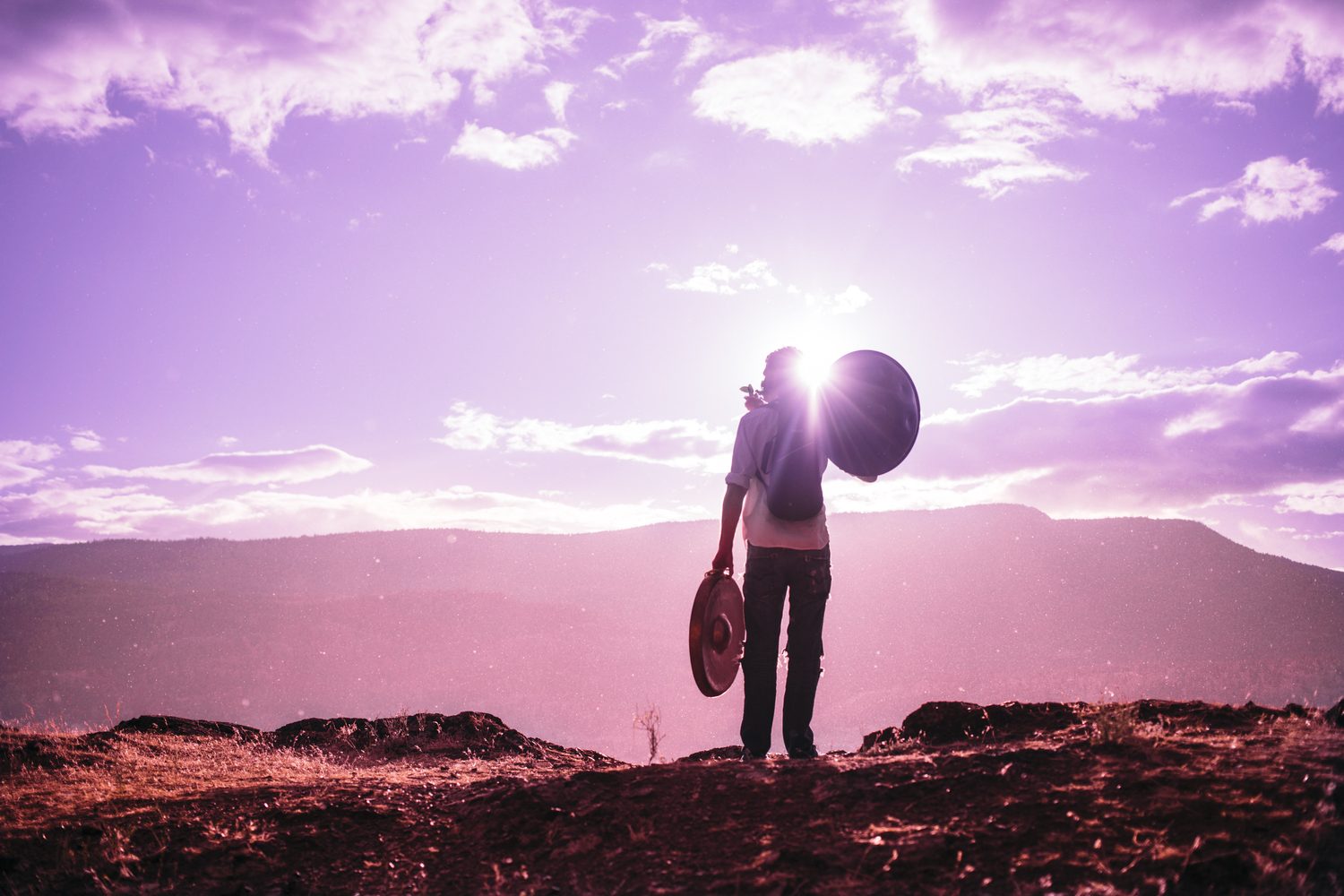Jacob silhouetted against a magenta sky and lake, holding a handpan and ukulele.