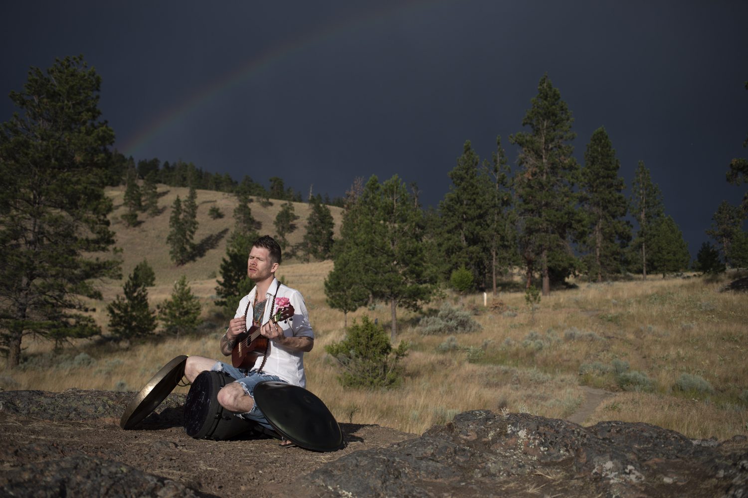 Jacob seated with a ukulele and instruments beneath a rainbow.