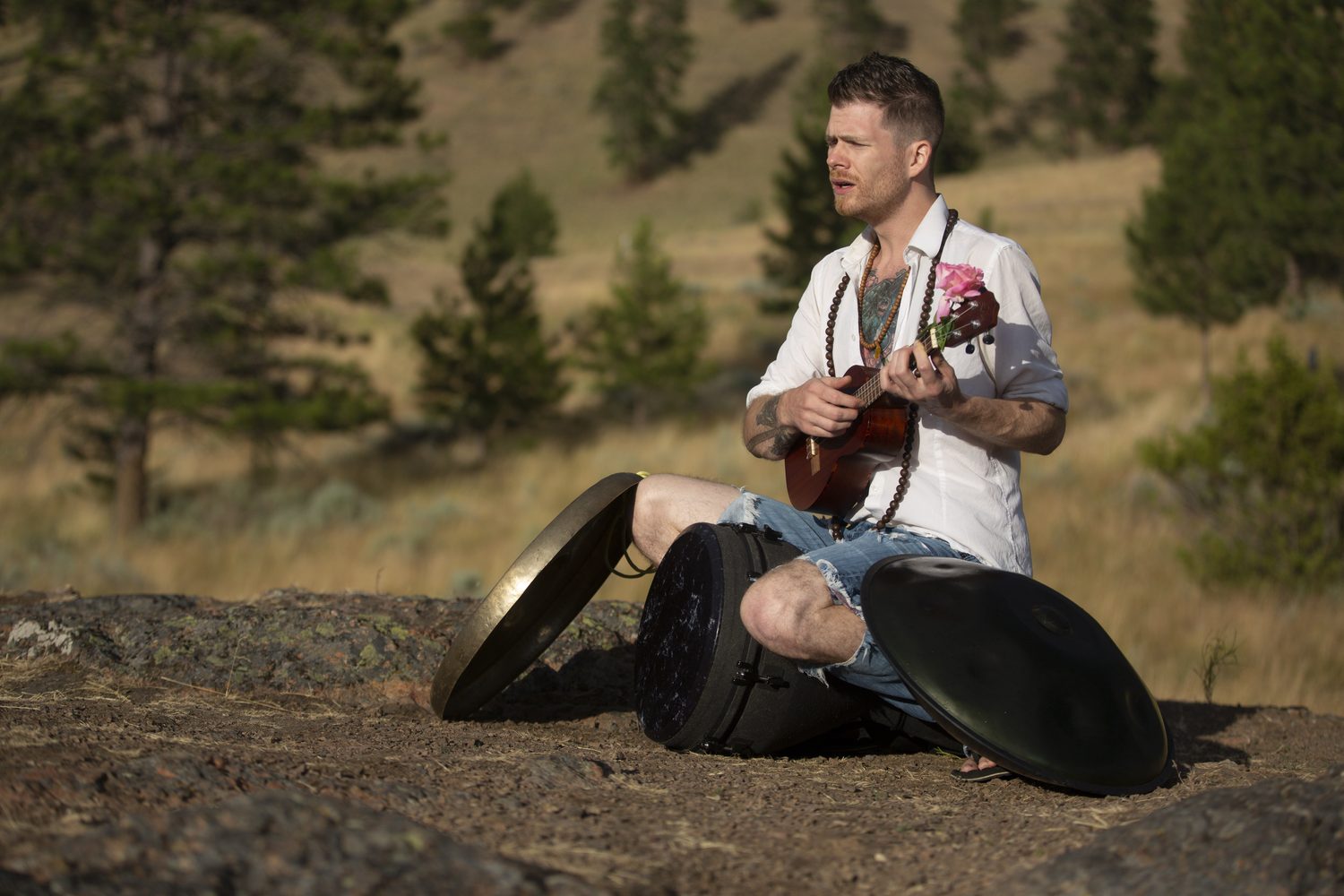 Jacob seated in the grass playing ukulele beside the instruments.