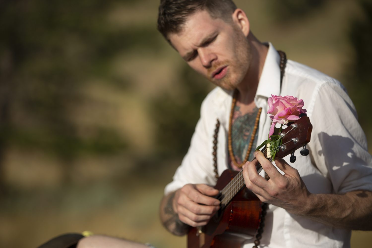 A close portrait of Jacob singing and playing ukulele with a rose.