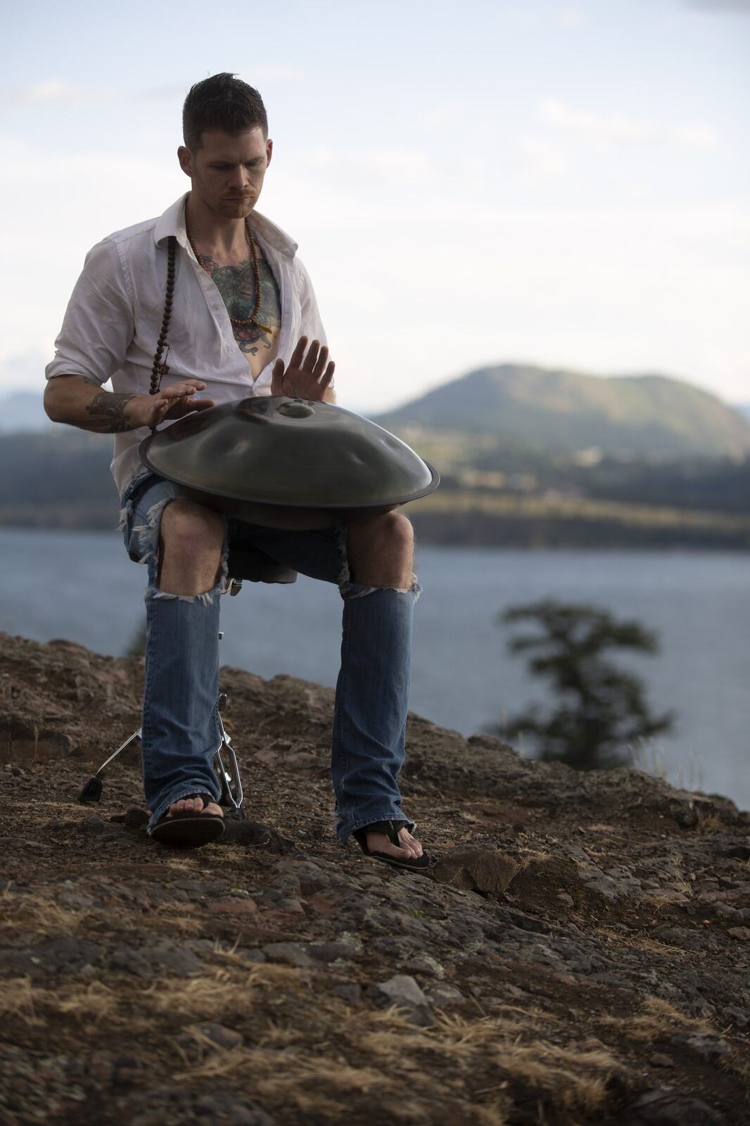 A vertical portrait of Jacob playing handpan at the lake overlook.