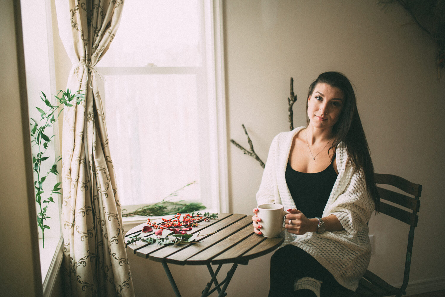 Jasmin seated beside a window with tea and winter greenery