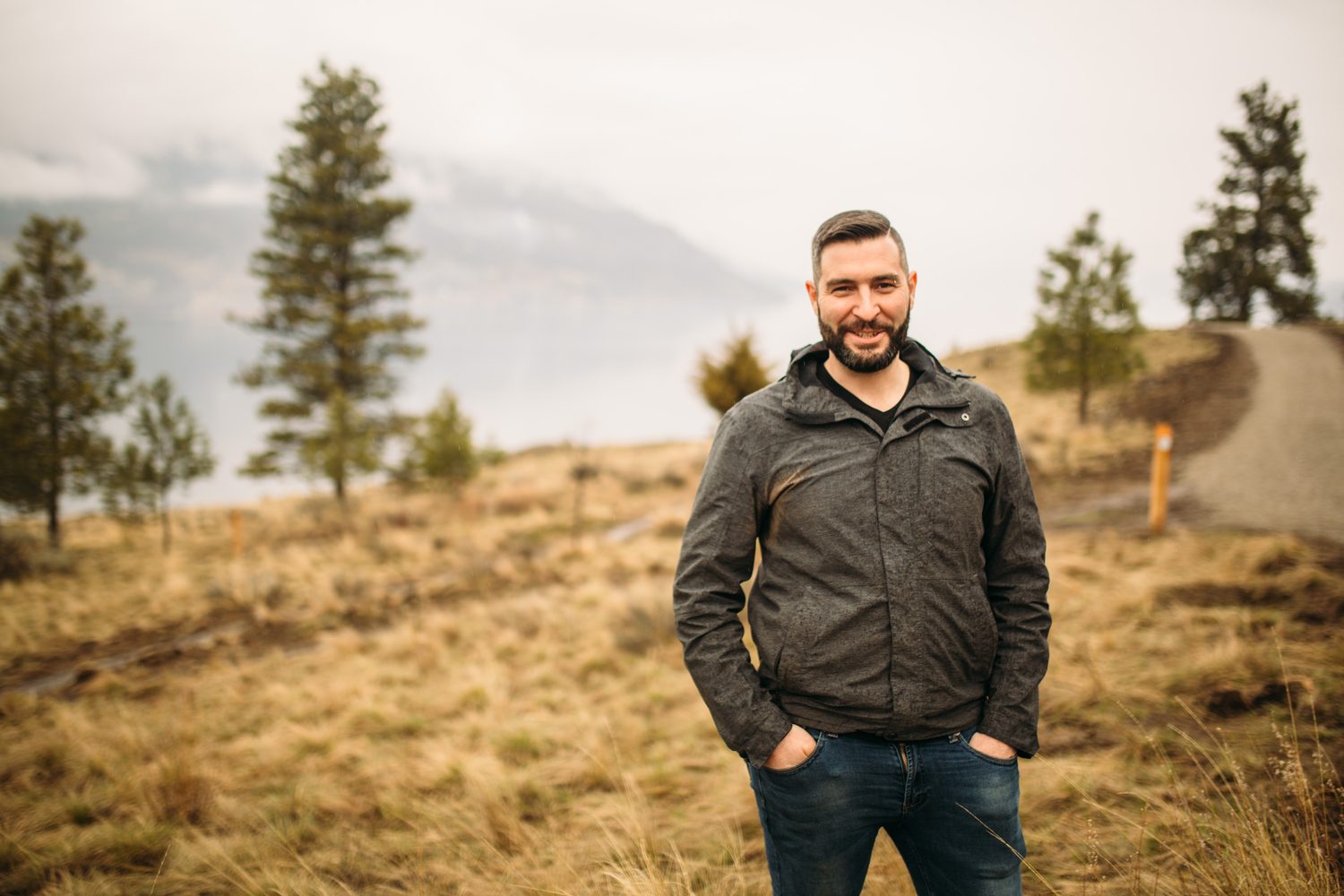 Very distant portrait of Jeremy standing alone in the Knox Mountain grassland.