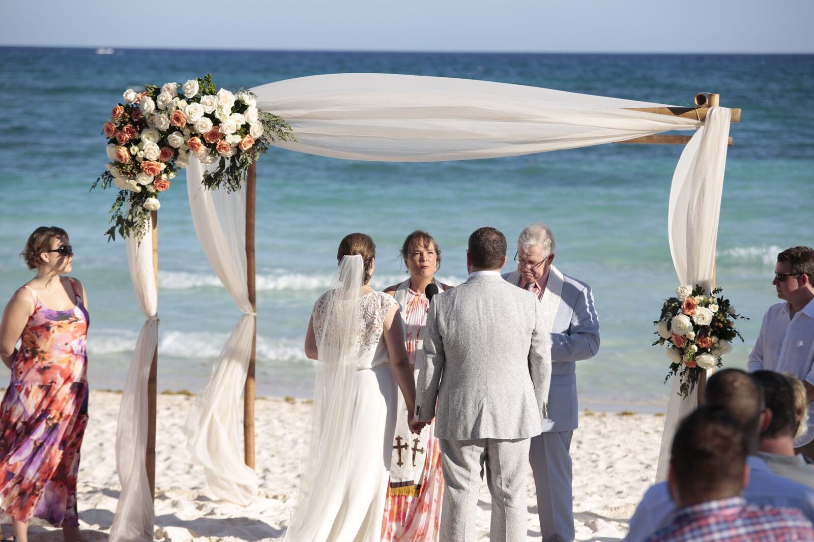 Kyra and Ted standing beneath the floral arch beside the Caribbean