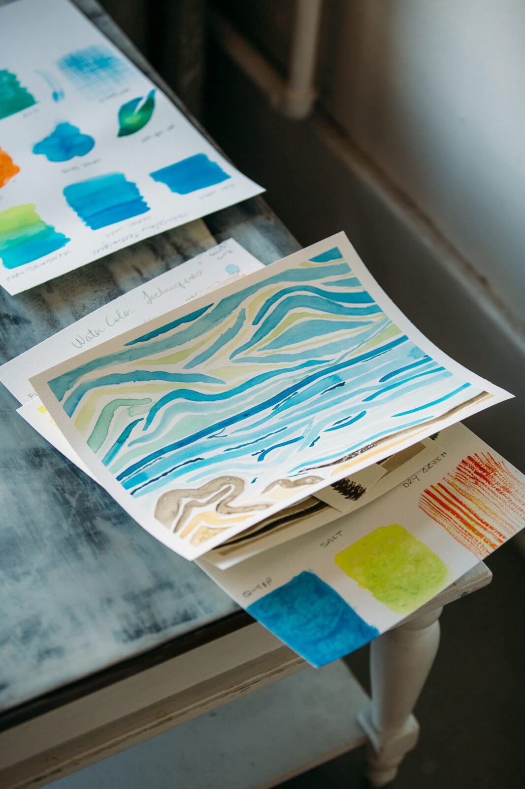 Finished blue and green watercolour practice sheets resting near a window.