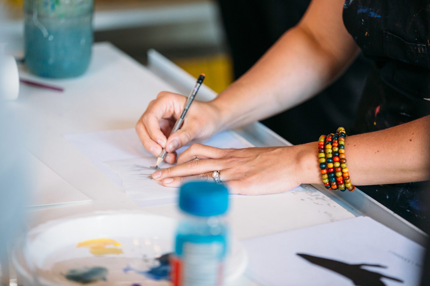 Hand sketching a watercolour outline beside a blue paint palette.