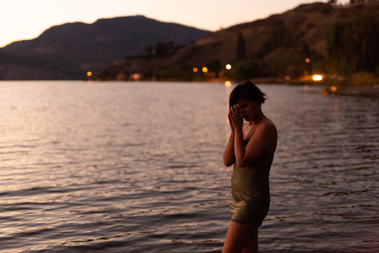 Lucy at the Water’s Edge portraits story frame 11: Lucy at the water’s edge as sunset slips into moonlight, moving from the shoreline and rocks to quiet close portraits and a warm-lit garden after dark. Photographed in Kelowna, BC.