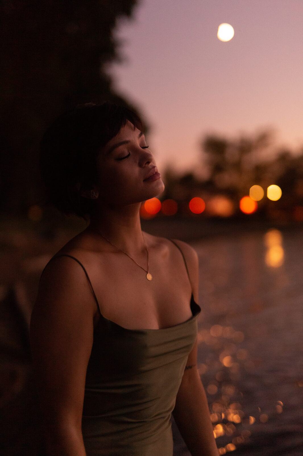 Lucy at the Water’s Edge portraits story frame 17: Lucy at the water’s edge as sunset slips into moonlight, moving from the shoreline and rocks to quiet close portraits and a warm-lit garden after dark. Photographed in Kelowna, BC.