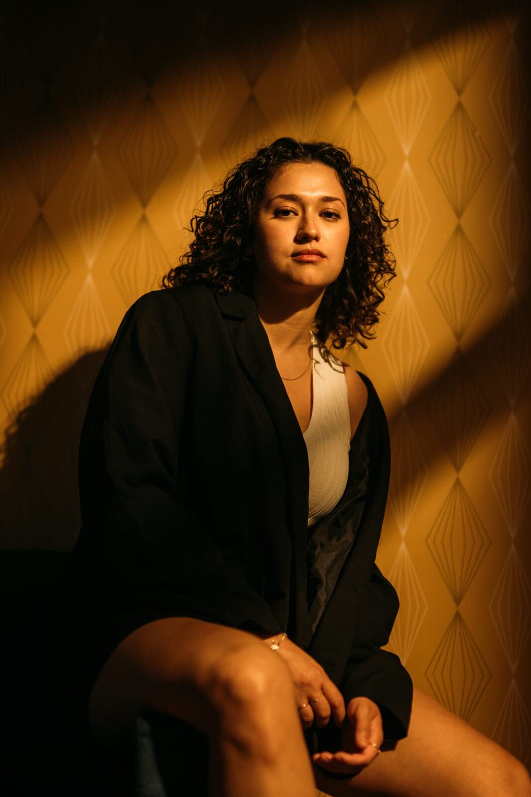 Marina in Warm Window Light portraits story frame 1: Marina in warm indoor light, with amber shadow, denim, black robe, green styling and an intimate editorial portrait mood.