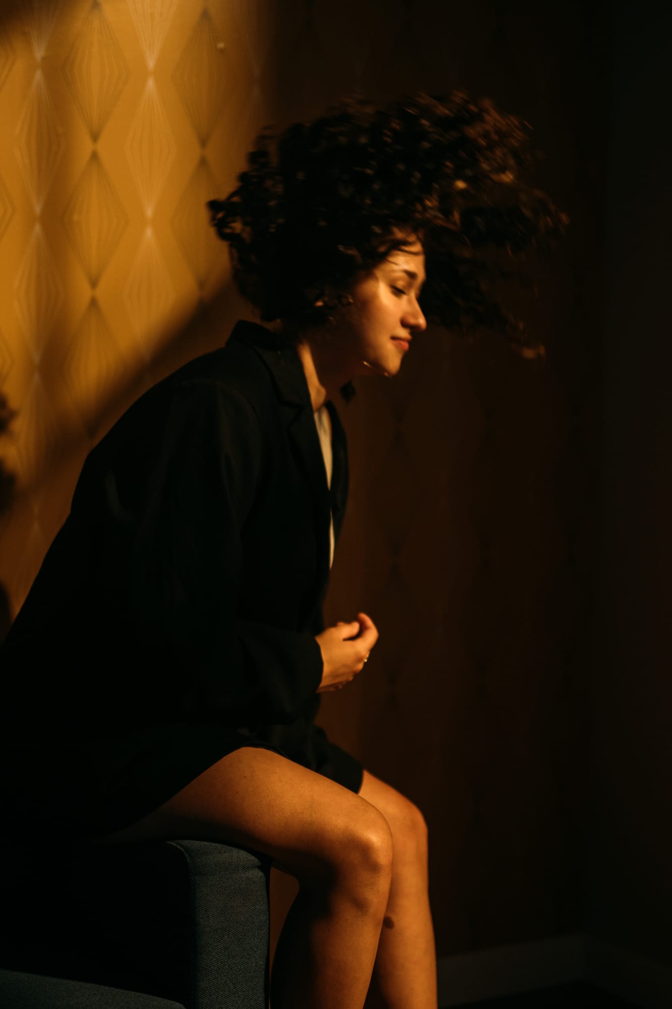 Marina in Warm Window Light portraits story frame 2: Marina in warm indoor light, with amber shadow, denim, black robe, green styling and an intimate editorial portrait mood.