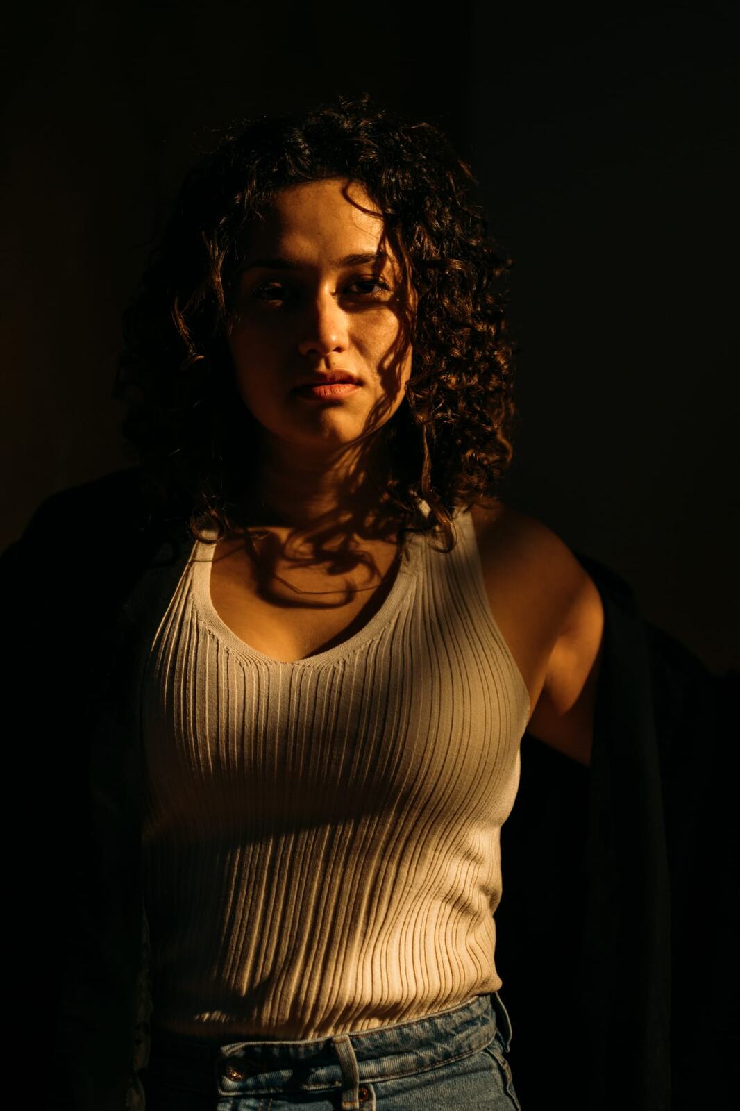 Marina in Warm Window Light portraits story frame 4: Marina in warm indoor light, with amber shadow, denim, black robe, green styling and an intimate editorial portrait mood.