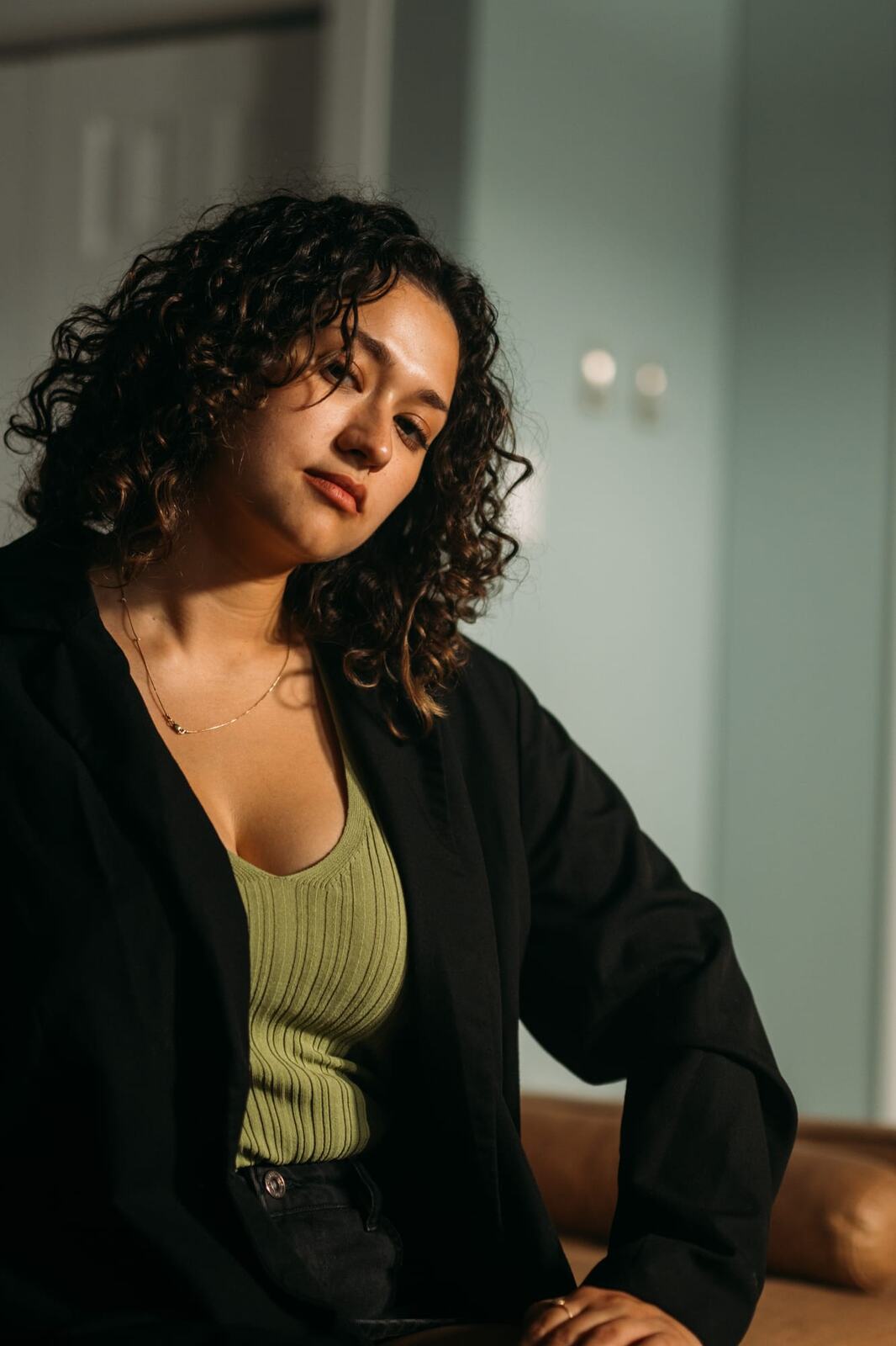 Marina in Warm Window Light portraits story frame 12: Marina in warm indoor light, with amber shadow, denim, black robe, green styling and an intimate editorial portrait mood.