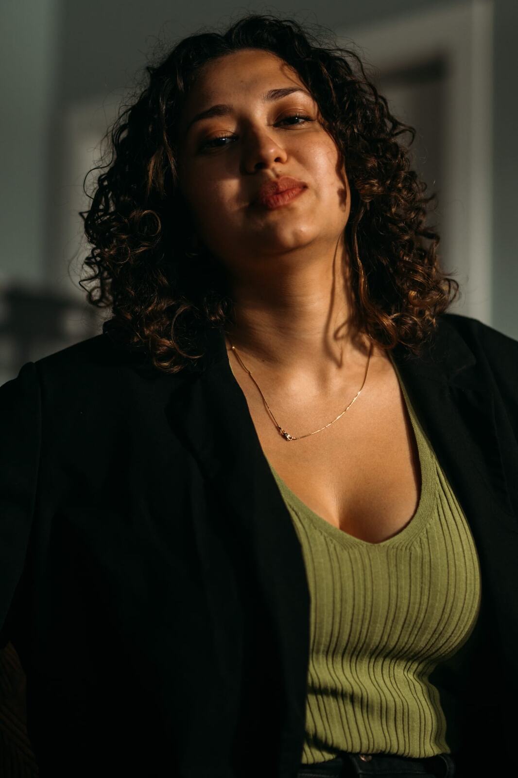 Marina in Warm Window Light portraits story frame 13: Marina in warm indoor light, with amber shadow, denim, black robe, green styling and an intimate editorial portrait mood.