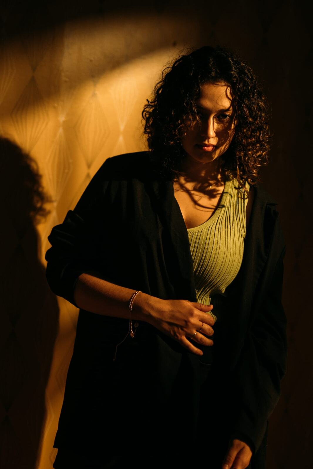 Marina in Warm Window Light portraits story frame 15: Marina in warm indoor light, with amber shadow, denim, black robe, green styling and an intimate editorial portrait mood.