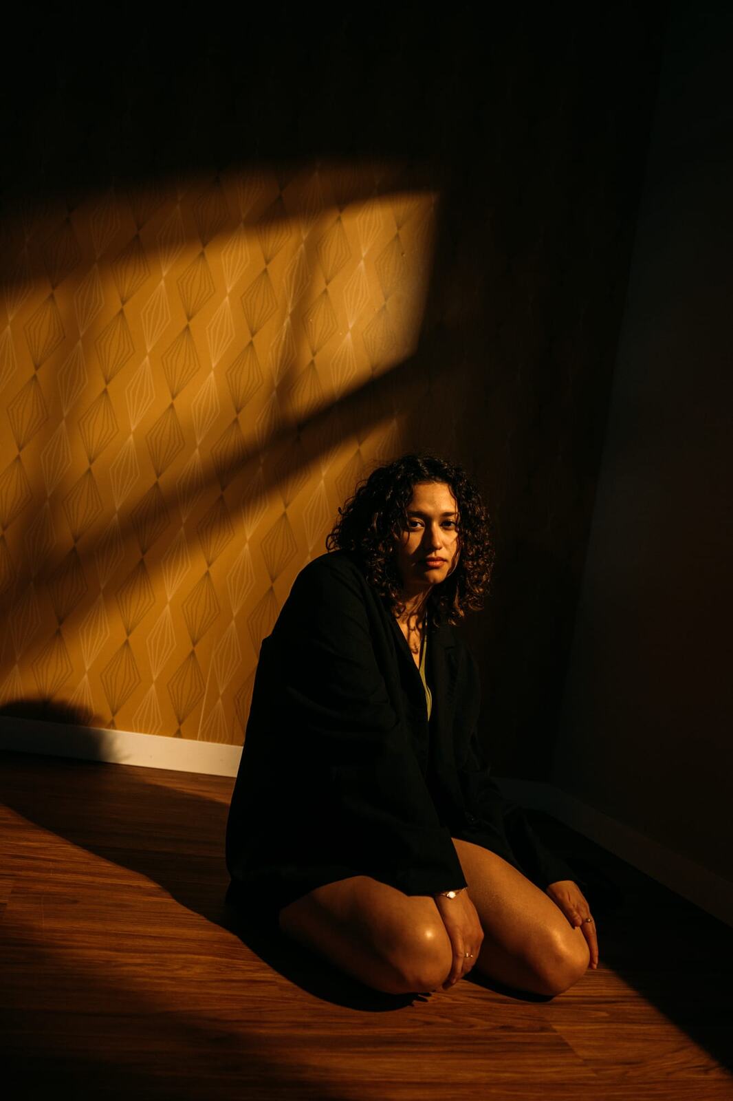 Marina in Warm Window Light portraits story frame 16: Marina in warm indoor light, with amber shadow, denim, black robe, green styling and an intimate editorial portrait mood.
