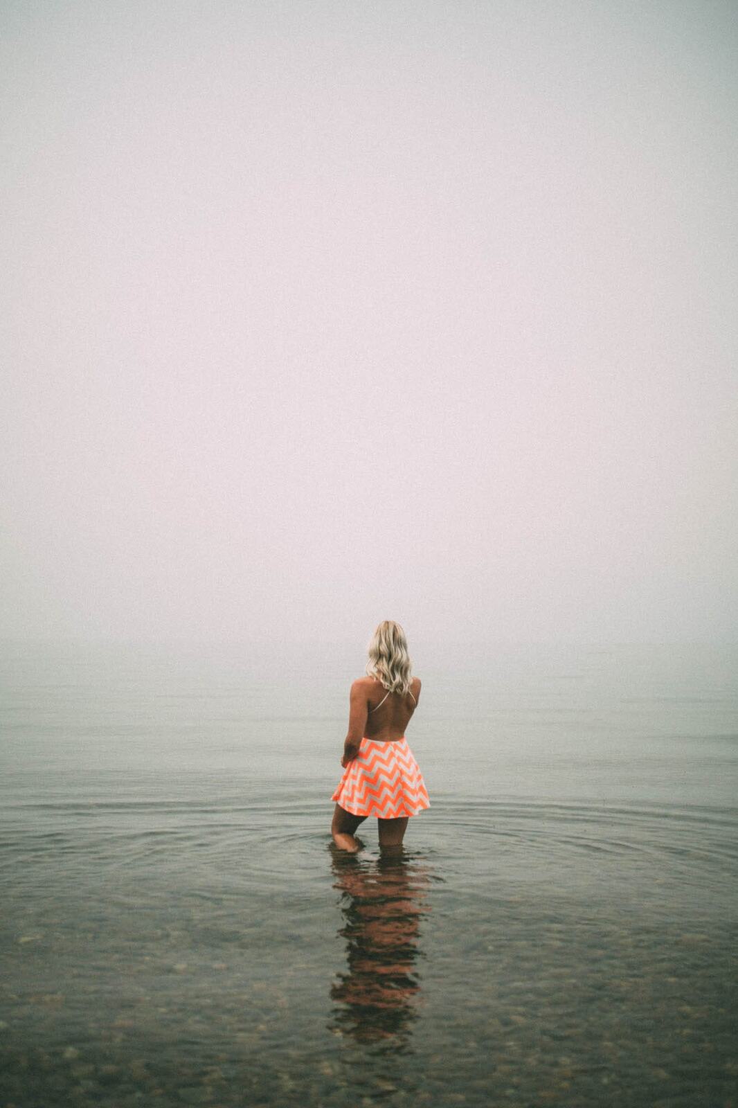 Megan Shallow portraits story frame 2: A fog-soft Kelowna lake portrait session for Megan Shallow, with water, orange dress movement, close body-language frames and quiet birds cutting through the mist.
