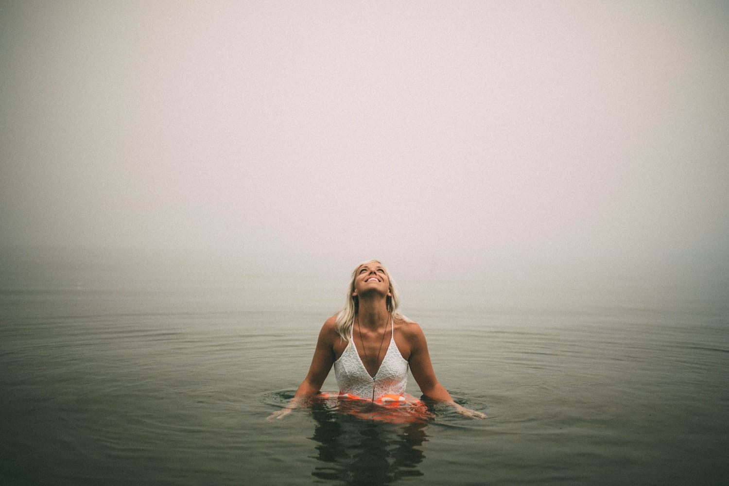 Megan Shallow portraits story frame 7: A fog-soft Kelowna lake portrait session for Megan Shallow, with water, orange dress movement, close body-language frames and quiet birds cutting through the mist.