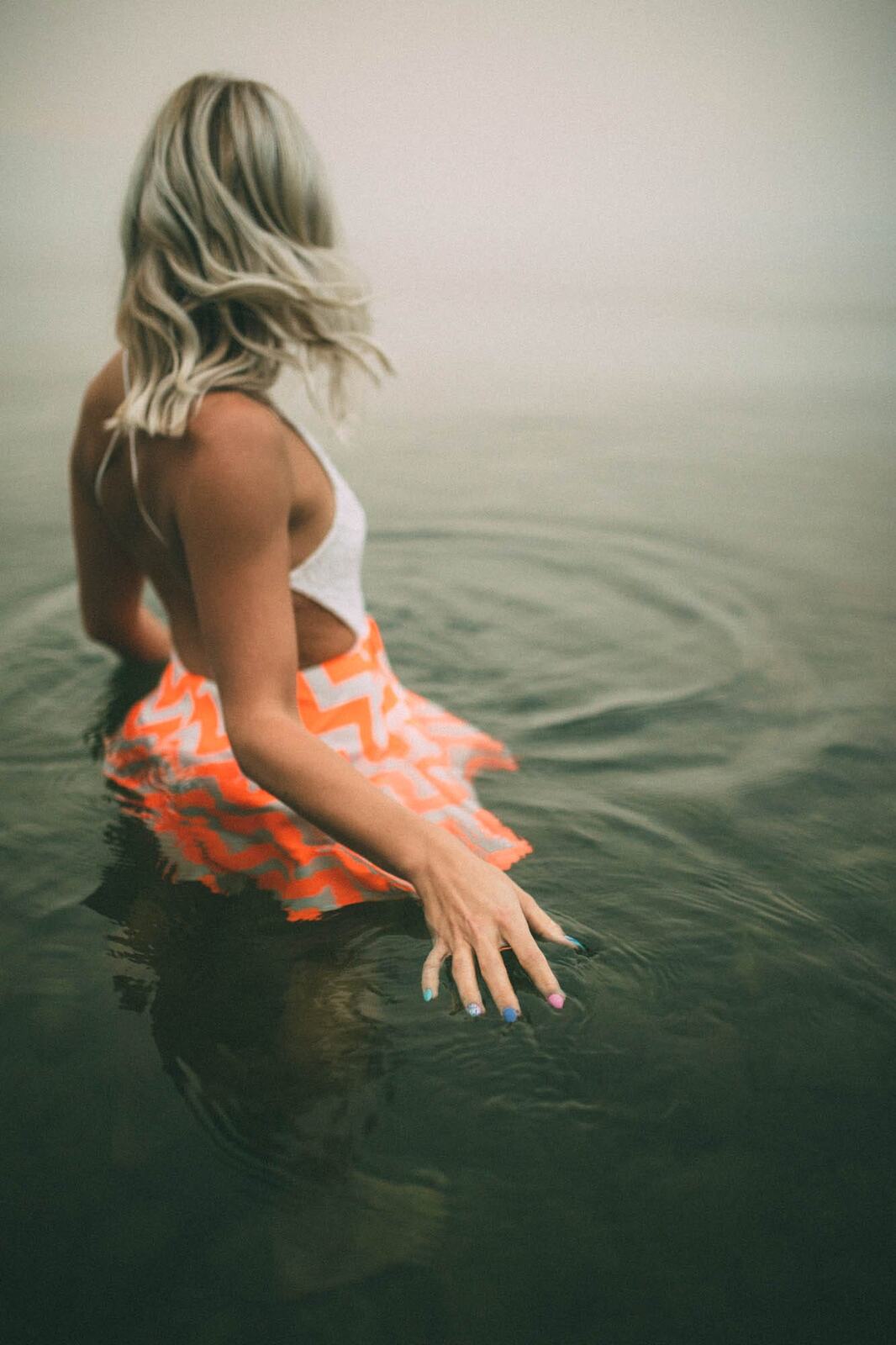 Megan Shallow portraits story frame 10: A fog-soft Kelowna lake portrait session for Megan Shallow, with water, orange dress movement, close body-language frames and quiet birds cutting through the mist.