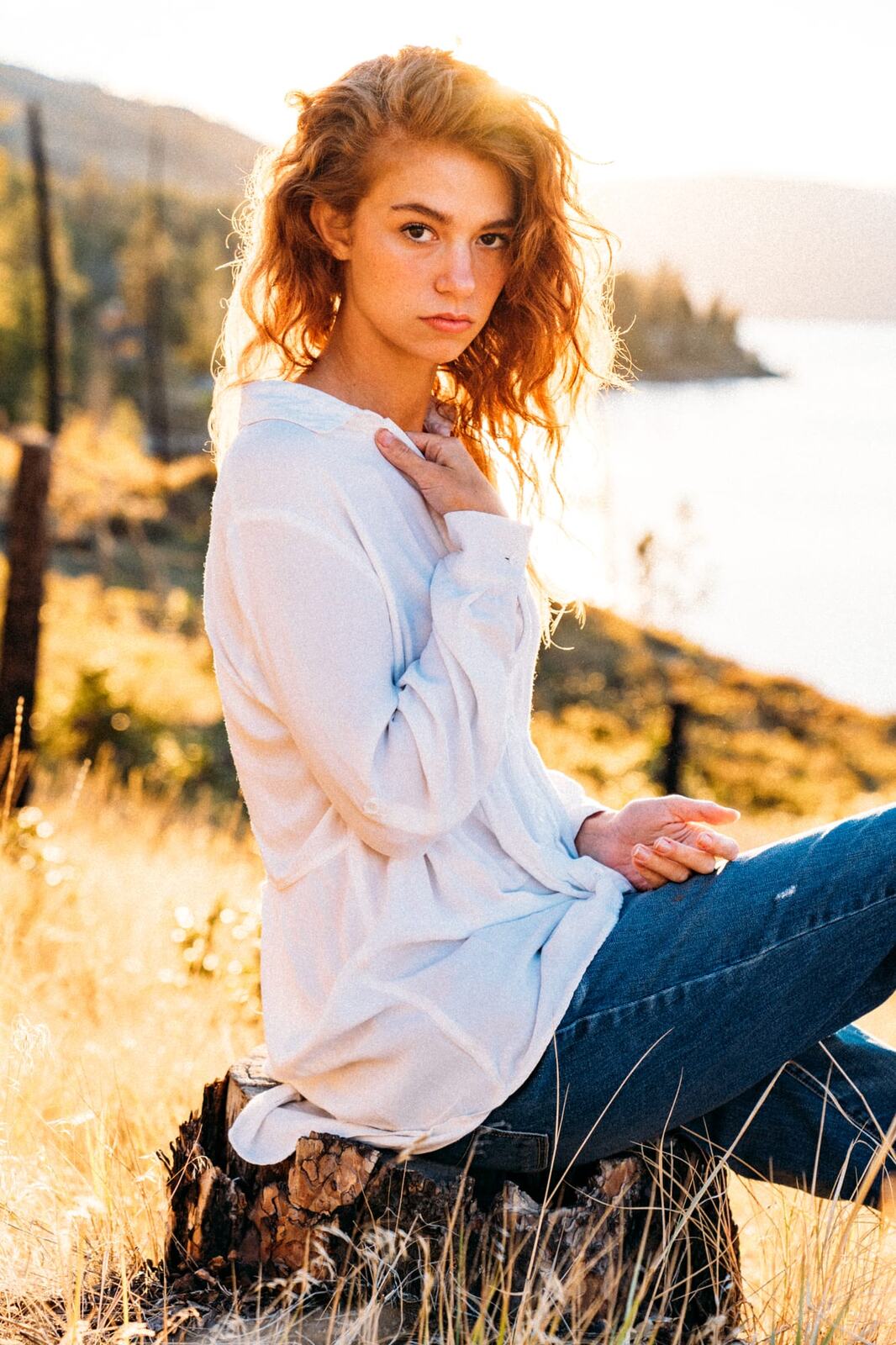 Mickie portraits story frame 2: A Kelowna portrait session for Mickie moving from golden grass and warm hillside light into lake-edge rocks, wind, white shirt styling and close editorial portraits.