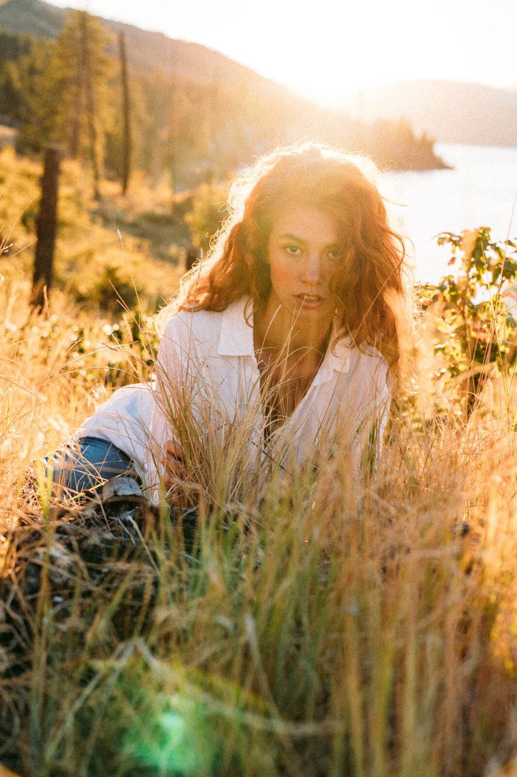 Mickie portraits story frame 3: A Kelowna portrait session for Mickie moving from golden grass and warm hillside light into lake-edge rocks, wind, white shirt styling and close editorial portraits.