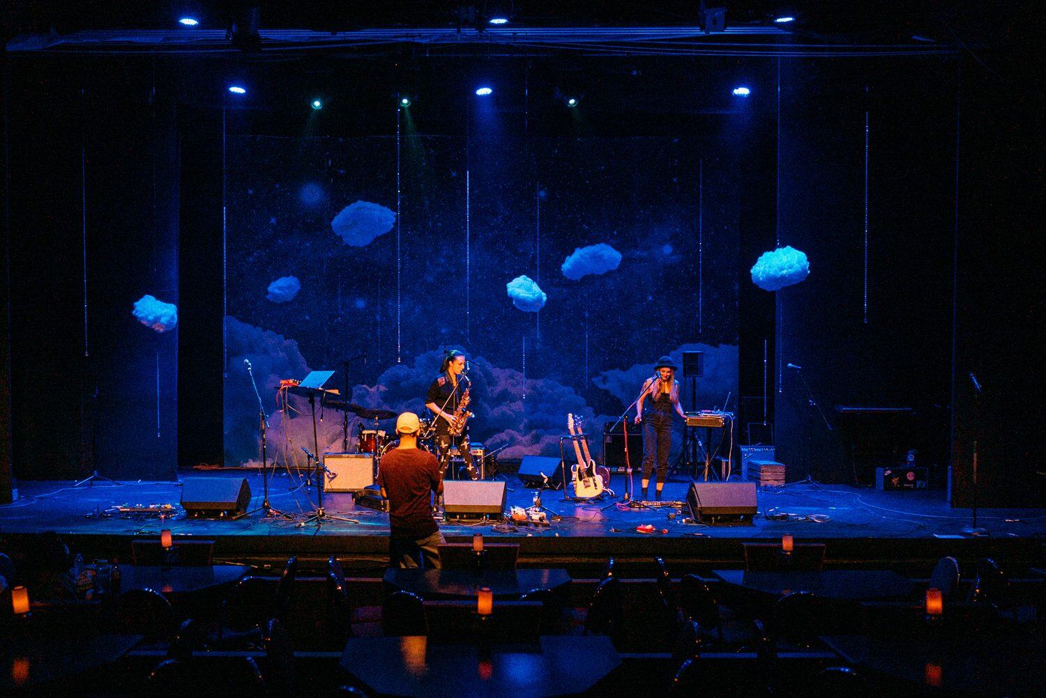 Smiling seated performer holding sticks beneath purple stage light.
