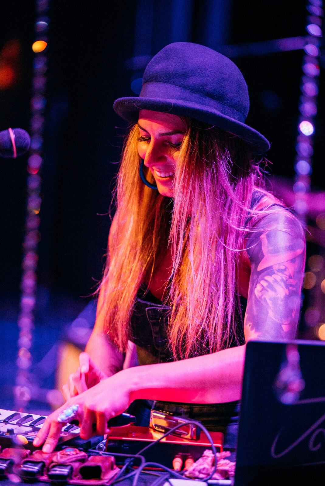Curly-haired guitarist playing under magenta light.