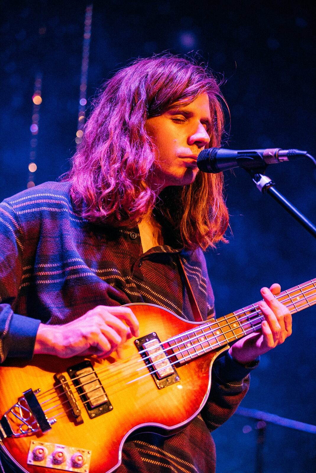 Wide blue-lit stage with a solo vocalist and instruments set at Kelowna Actors Studio.