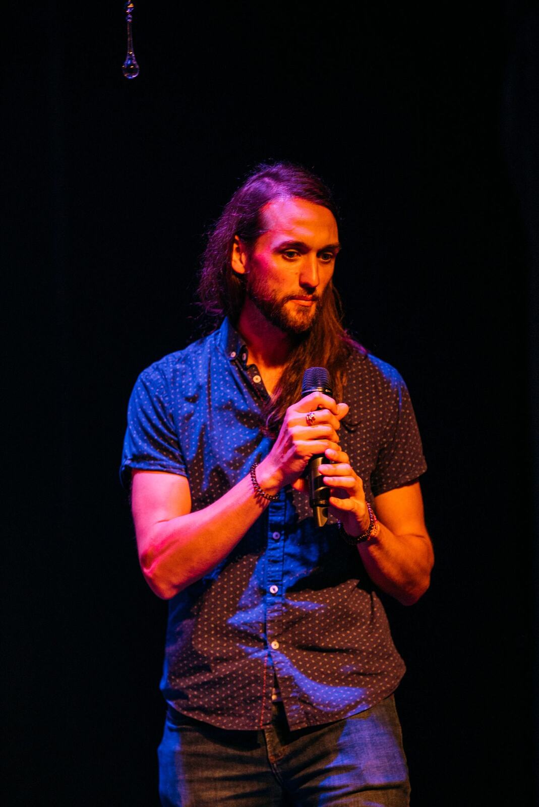 Wide blue-lit stage with a solo vocalist and instruments set at Kelowna Actors Studio.