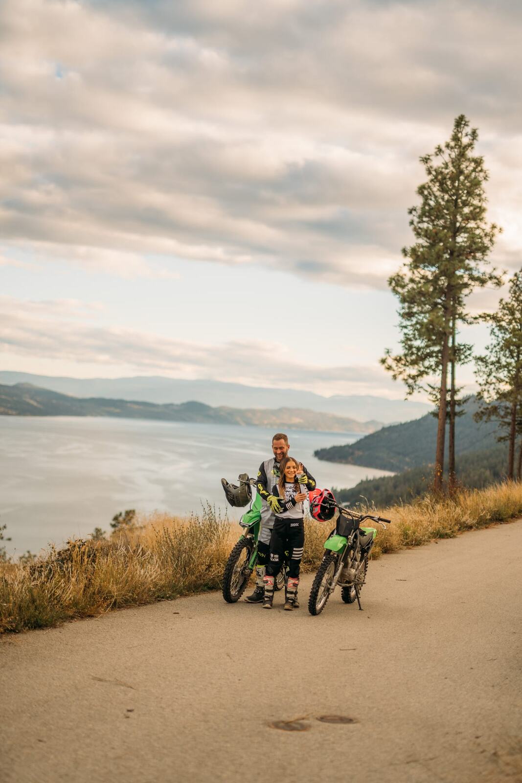 Rachel and Ryan portraits story frame 4: Okanagan couples portraits with dirt bikes, lake and mountain views, autumn sun, standing portraits and champagne celebration.