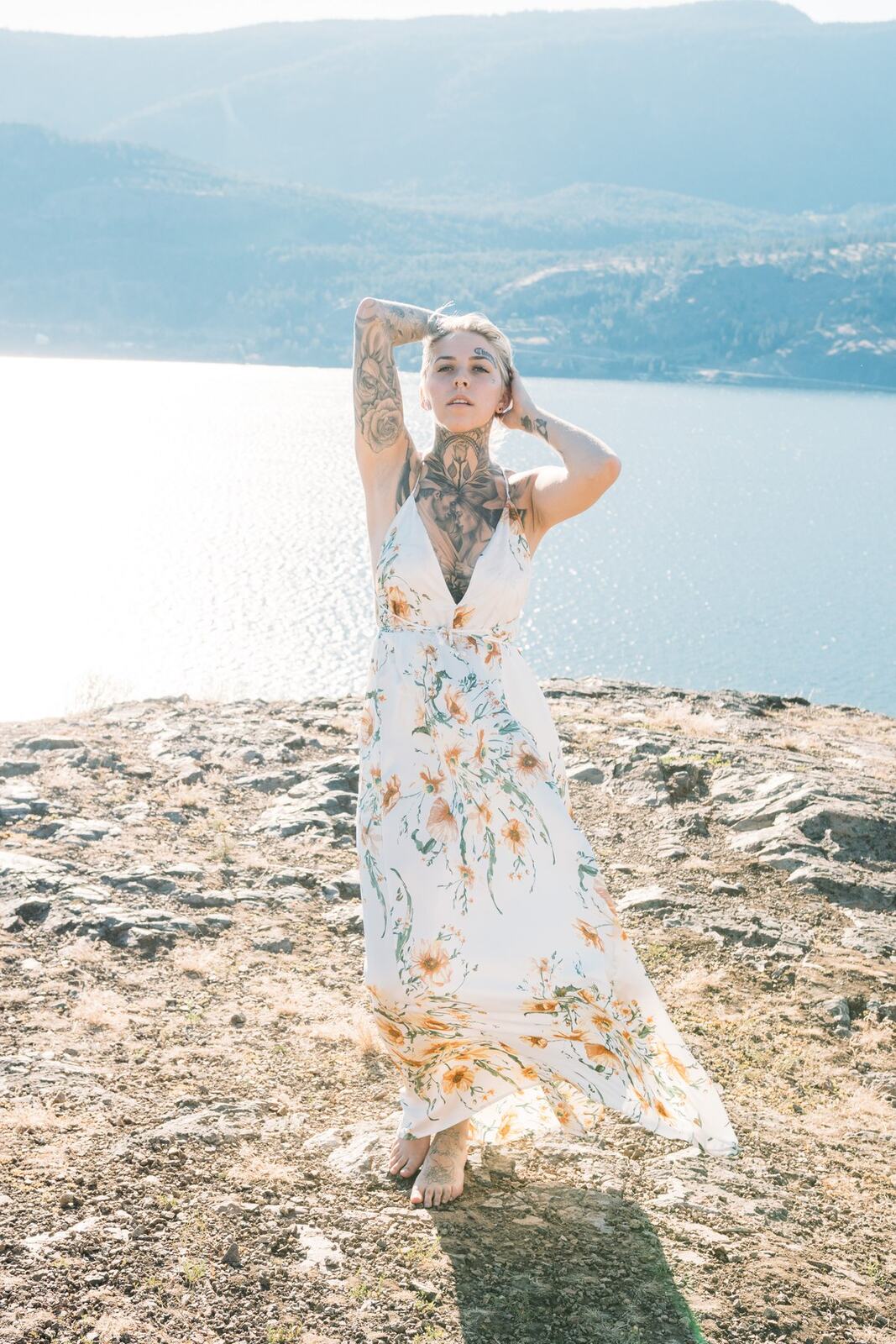 Rayleigh by Knox portraits story frame 1: Knox Mountain portraits in Kelowna with white floral dress, tattoo detail, reeds, water, sunlight and a stronger summer edge.