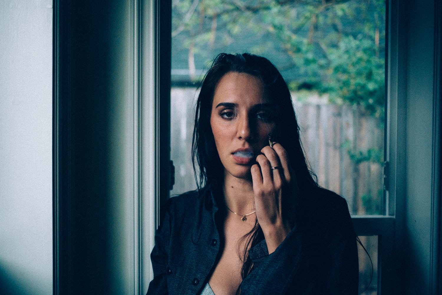 Rebecca in Smoke portraits story frame 20: A dark Kelowna portrait story for Rebecca with window light, smoke, denim, close expression and a low-key editorial mood.