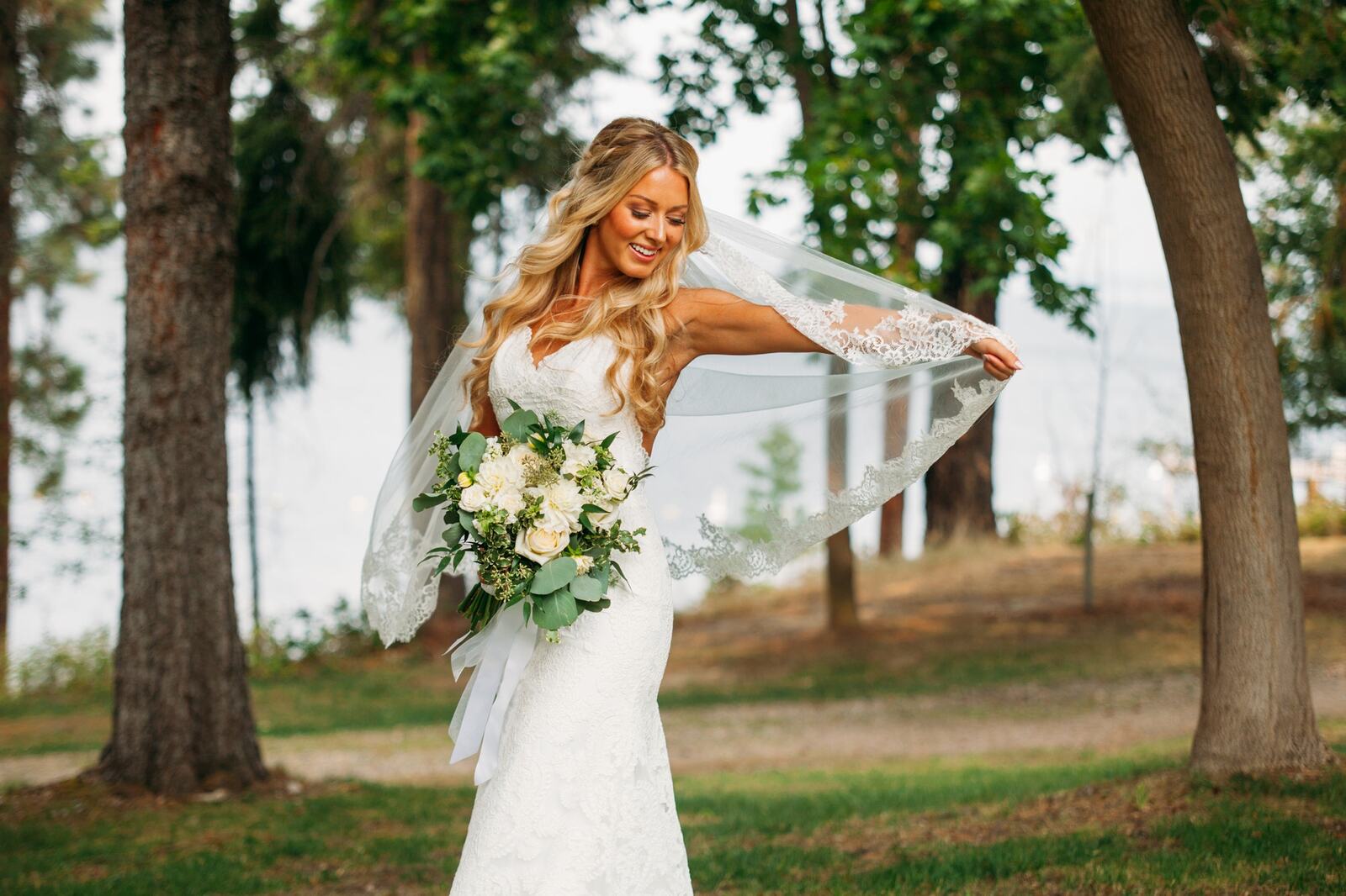 Sarah holding her veil beside trees and water