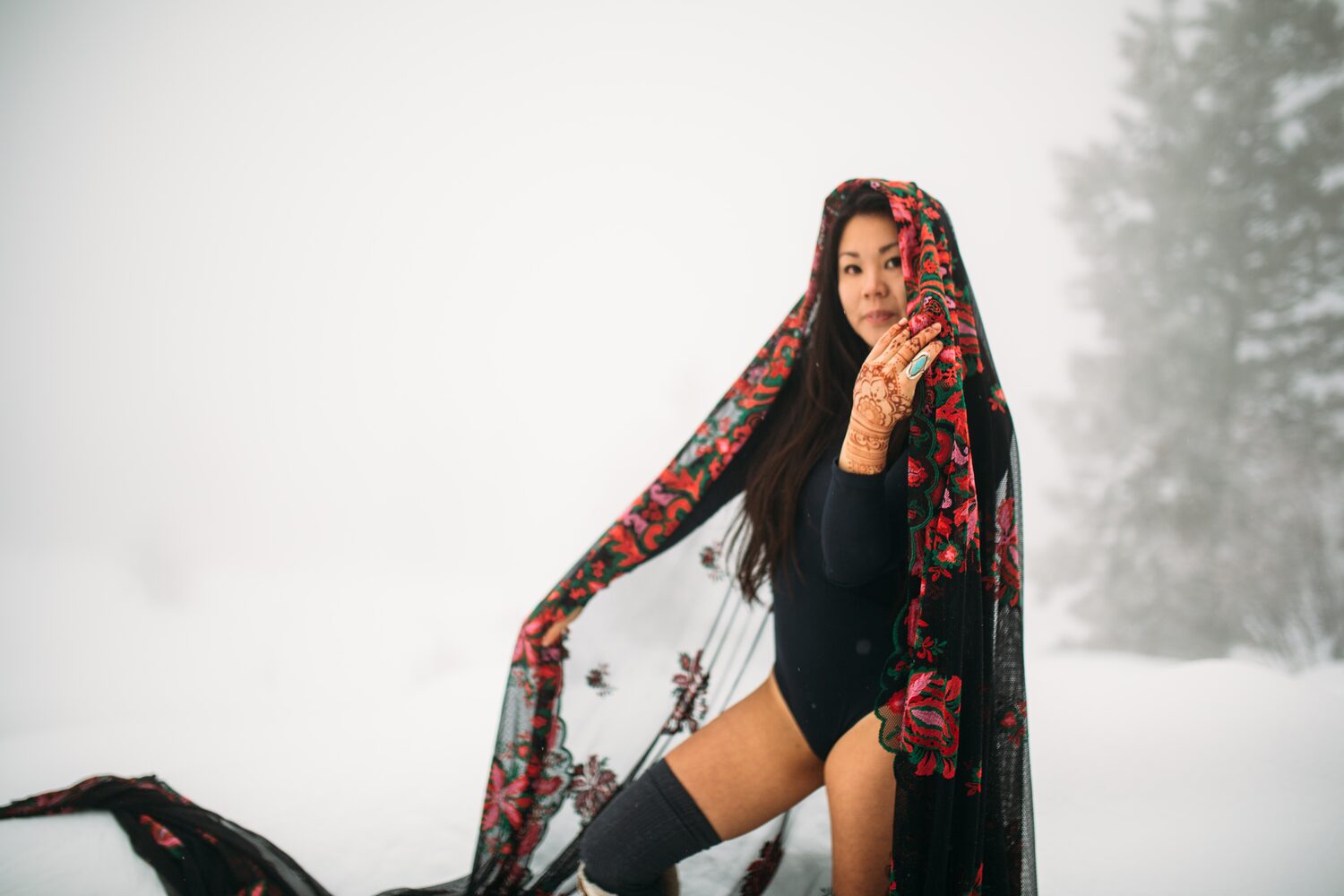 Sarah in the snow, framed by sheer floral fabric with her henna visible